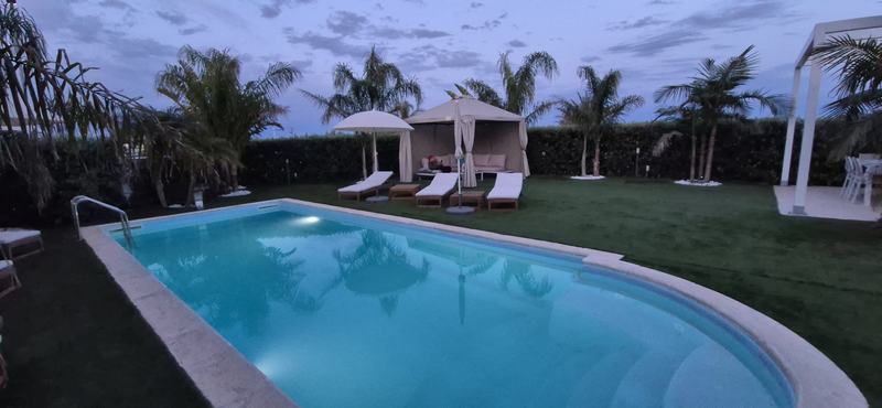 Piscina al tramonto tra palme, ombrelloni e gazebo