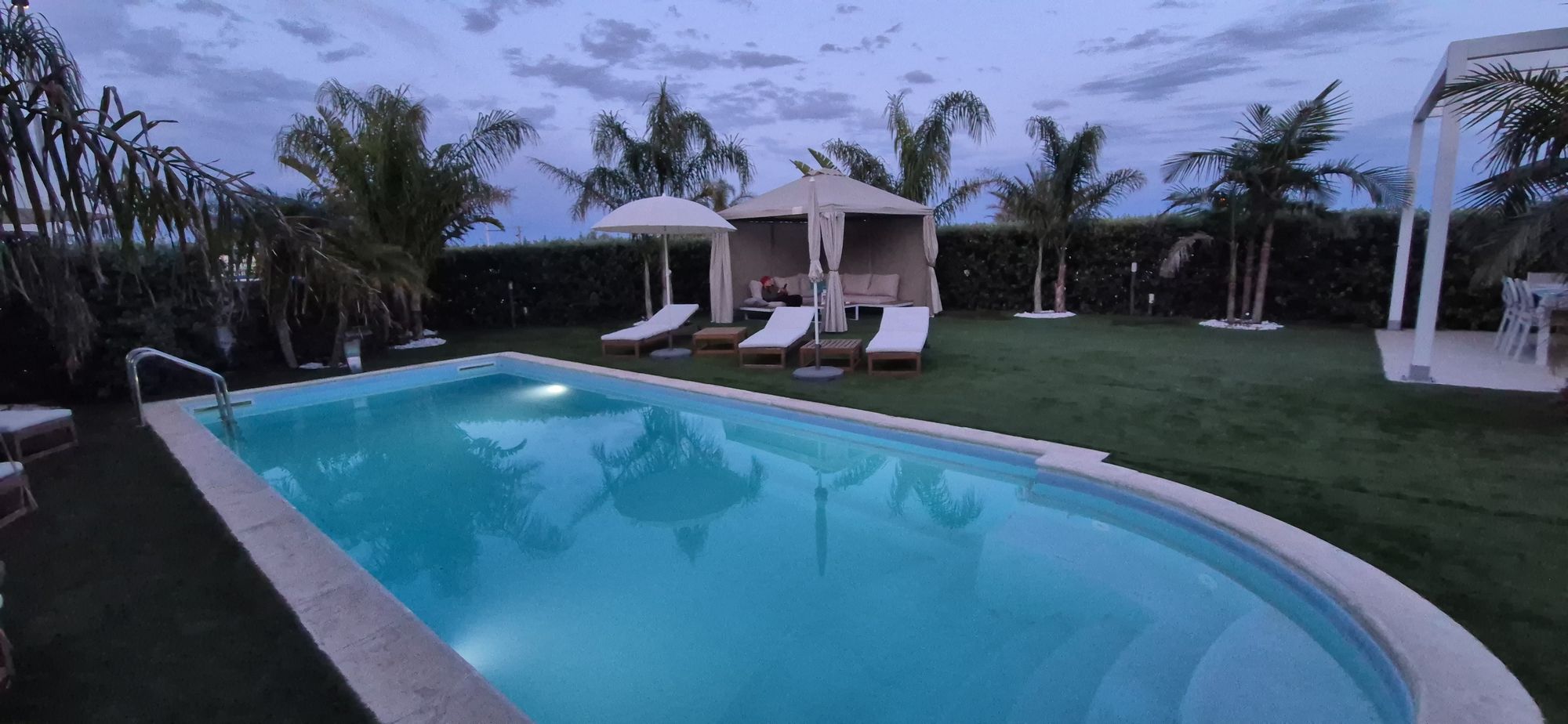 La piscina di Villa Gisira al tramonto, tra palme, ombrelloni e gazebo