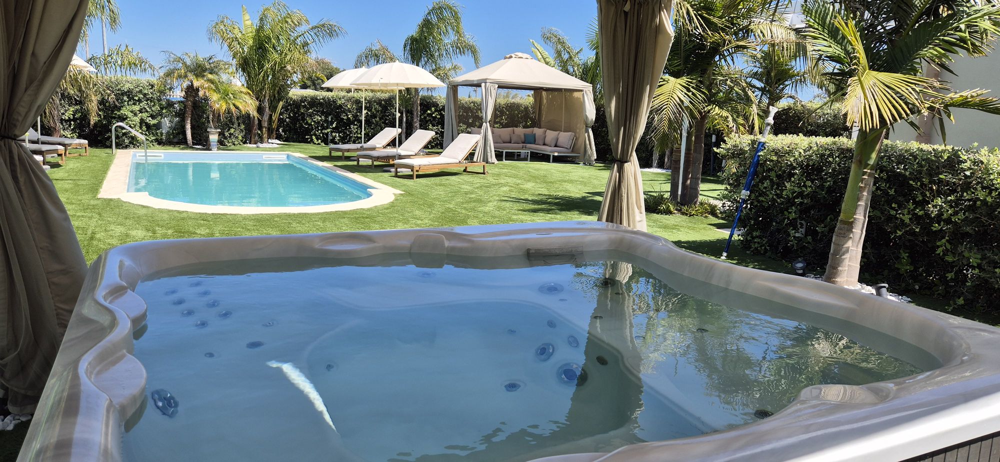 Jacuzzi in primo piano con la piscina e i lettini sullo sfondo