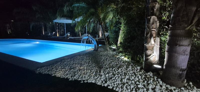 Piscina illuminata di notte tra palme e ciottoli